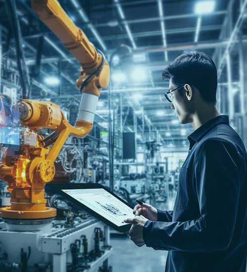 A manufacturing engineer working beside a robotic arm on the factory floor.